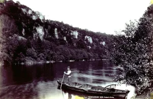 Mountain River Scenery Drucke: A stretch of river surrounded by mountains. In the foreground a rowboat and its owner