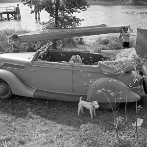 Ein Mann und eine Frau tragen ein Klepper Faltboot an einem Ford V8 Cabrio vorbei an Land, Deutschland 1930er Jahre.