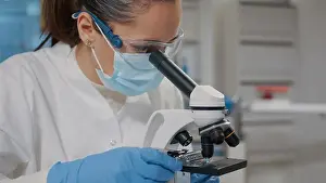 Microscope Laboratory Equipment Drucke: Biologist with face mask using microscope in science laboratory