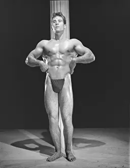 Black And White Muscular Men Drucke: Bodybuilder Poses In Front Of Pole c.1954