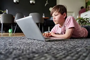 2020 Drucke: Junge liegt auf dem Boden, arbeitet an Laptop.