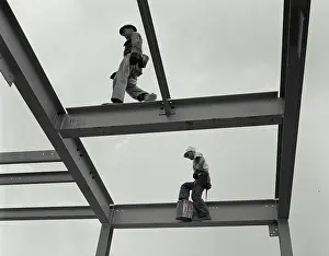 Low Angle View Photography Drucke: Two construction workers walking on the frame of a grain elevator