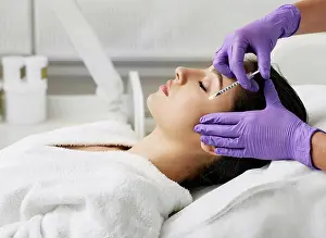 Drucke von Ein Arzt injiziert eine Lösung in das Gesicht einer Frau, um Falten und Altersflecken zu reduzieren Februar Drucke: Faciale Mesotherapie