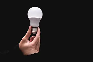Light Bulb Concept Drucke: light bulb in hand on a black background