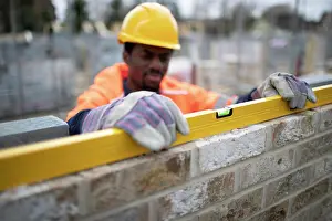 Building Site Safety Drucke: Male construction worker using level tool on brick wall