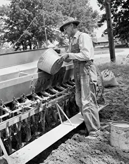 Black And White Agriculture Drucke: Mature man loading grinds into sowing machine