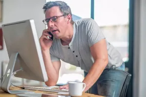 Man Using Smartphone Drucke: Man at computer using smartphone to make telephone call