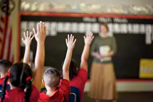 2019 Drucke: Schüler mit erhobenen Händen in einem Klassenzimmer.