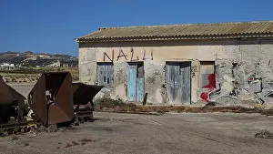 Landschaftsmalerei Drucke: Verlassenes Gebäude mit Graffiti und rostigem Gerät unter klarer Himmel.