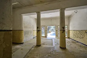 Drucke von Ein verlassener Gang mit Säulen, Graffiti an den Wänden und Tageslicht, das durch die offenen Türen strömt, Verlorener Ort, ehemaliges Sanatorium, Tuberkulosezentrum 1947-1970 Malerei Drucke: Ein verlassener Gang mit Säulen.