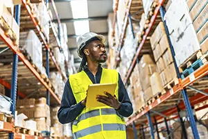 Industrial Supply Chain Management Drucke: African warehouse supervisor using tablet while working tracking packages and doing inventory