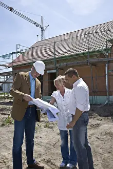 Construction Industry Workforce Drucke: Architect and married couple looking at a construction plan in front of framing