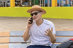 Young Man On Phone Drucke: An attractive guy calling on a cell phone on a bench