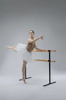 Ballet Dancer Pose Drucke: A ballet dancer in a white tutu performs an elegant pose by the barre in a dance studio