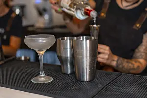Female Bartender At Work Drucke: Bartender using a measuring tool to prepare a cocktail in the counter of a bar