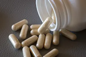 Beige Capsules Drucke: Beige capsules roll out of an open bottle onto a dark surface