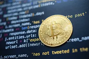 Cryptocurrency Symbol Drucke: Bitcoin coin placed on top of a black screen filled with colorful programming code