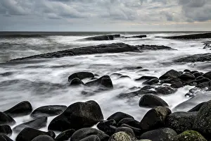 Rocky Shoreline England Drucke: Black, round rocks in the surf