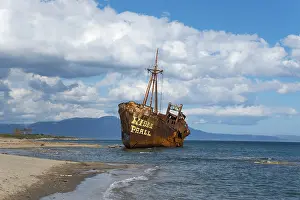 Peloponnese Coastline Drucke: The bow of a rusty ship eats into the sandy beach against a blue sky and fluffy clouds