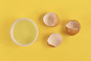 Clearable Food Images Drucke: Bowl with egg white next to broken eggshells on yellow background