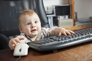 Young Boy At Desk Drucke: Boy, 10 months, using a computer mouse and keyboard