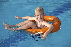 Boy Looking At Camera Drucke: Boy, 7, in a pool on a life ring