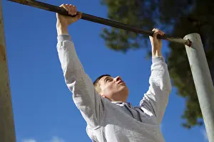 Young Man Training Drucke: The boy pulls himself up on the horizontal bar on the street