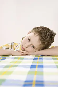 Studio Shot Of A Child Drucke: Boy sitting at a table, bored