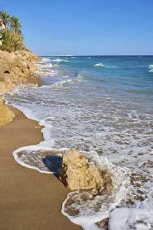 Steep Coastline In Southern Europe Drucke: Breaking waves on a sandy beach with a rock