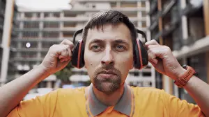 Construction Worker Safety Drucke: Builder covers his ears, ear muff to protect workers ears