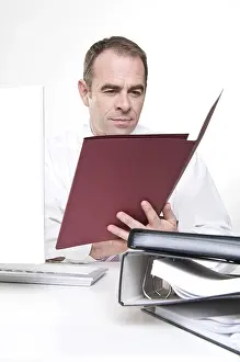 Office Work Attire Drucke: Businessman sitting at computer looking at a file