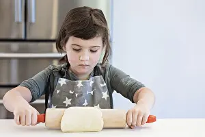 Happy Child Cooking Drucke: A child in a star patterned apron rolls out dough with concentration