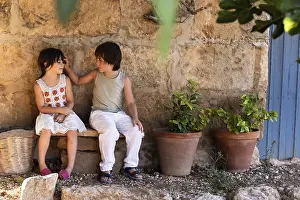 Childhood Friendship Drucke: Two children sit on a stone bench by a rustic wall