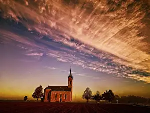 Bilder Datiert 23. Oktober 2024: Eine Kirche umgeben von Bäumen bei einem dramatischen Sonnenuntergang.
