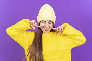 Happy Adult Female Face Drucke: Close up portrait of a young, cheerful woman isolated on purple studio background in yellow woolen pullover smiling