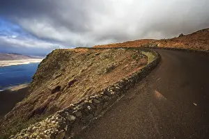 Rocky Coastline Africa Drucke: Coastal road along a dramatic cliff under a cloudy sky