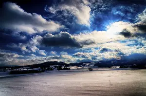 Central European Winter Scenes Drucke: Colourful winter landscape with dramatic clouds and sun rays over snow-covered fields
