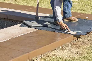 Male Construction Worker Drucke: Construction worker applying pressure to texture template on wet cement