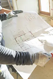 Interior Architecture Drucke: A construction worker holds a construction plan in his hands in a light-filled room