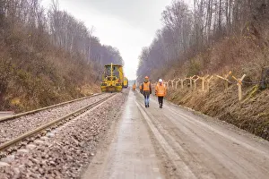 Railway Construction Site Drucke: Construction worker and machine tool working on a railroad track in the forest