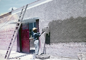Red Coloured Building Structure Drucke: Construction worker throwing cement through a sieve to make wall panelling over modern red bricks