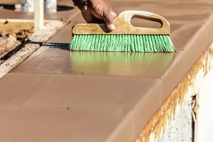 Contractor Services Near Me Drucke: Construction Worker Using Brush On Wet Cement Forming Coping Around New Pool