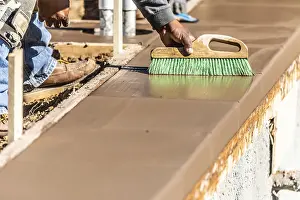 Building Construction Process Drucke: Construction worker using brush on wet cement forming coping around new pool