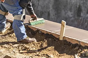 Construction Industry Workforce Drucke: Construction worker using brush on wet cement forming coping around new pool