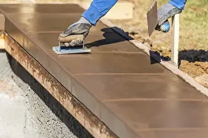 Building Construction Site Drucke: Construction worker using hand groover on wet cement forming coping around new pool