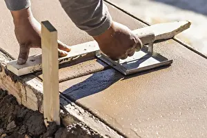 One Person Construction Team Drucke: Construction worker using hand groover on wet cement forming coping around new pool