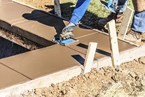 Construction Industry Workforce Drucke: Construction worker using hand groover on wet cement forming coping around new pool