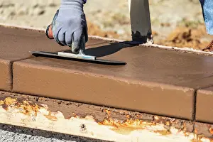 Swimming Pool Building Drucke: Construction Worker Using Trowel On Wet Cement Forming Coping Around New Pool