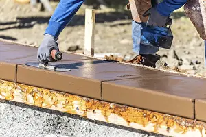 Construction Industry Workforce Drucke: Construction worker using trowel on wet cement forming coping around new pool