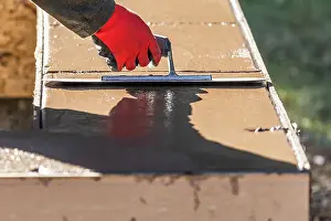 Swimming Pool Building Drucke: Construction Worker Using Trowel On Wet Cement Forming Coping Around New Pool